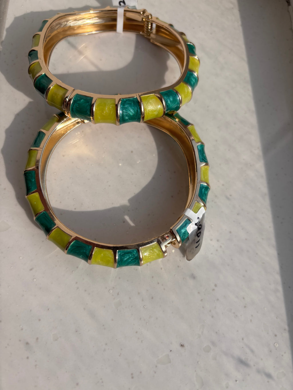 A pair of gold-plated bangle bracelets decorated with alternating green and yellow rectangular enamel tiles, resting on a light-colored surface.