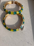 A pair of gold-plated bangle bracelets decorated with alternating green and yellow rectangular enamel tiles, resting on a light-colored surface.