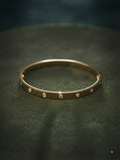 A slim gold bangle bracelet with small inset clear stones spaced around the band, photographed on a dark textured surface.
