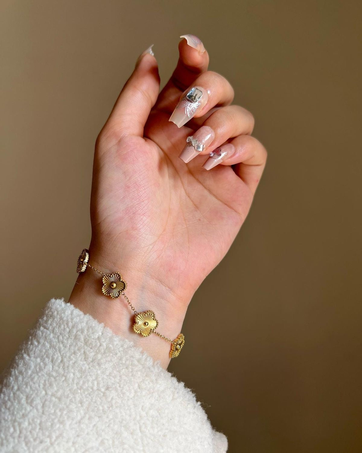 Hand wearing a gold bracelet with a plain background
