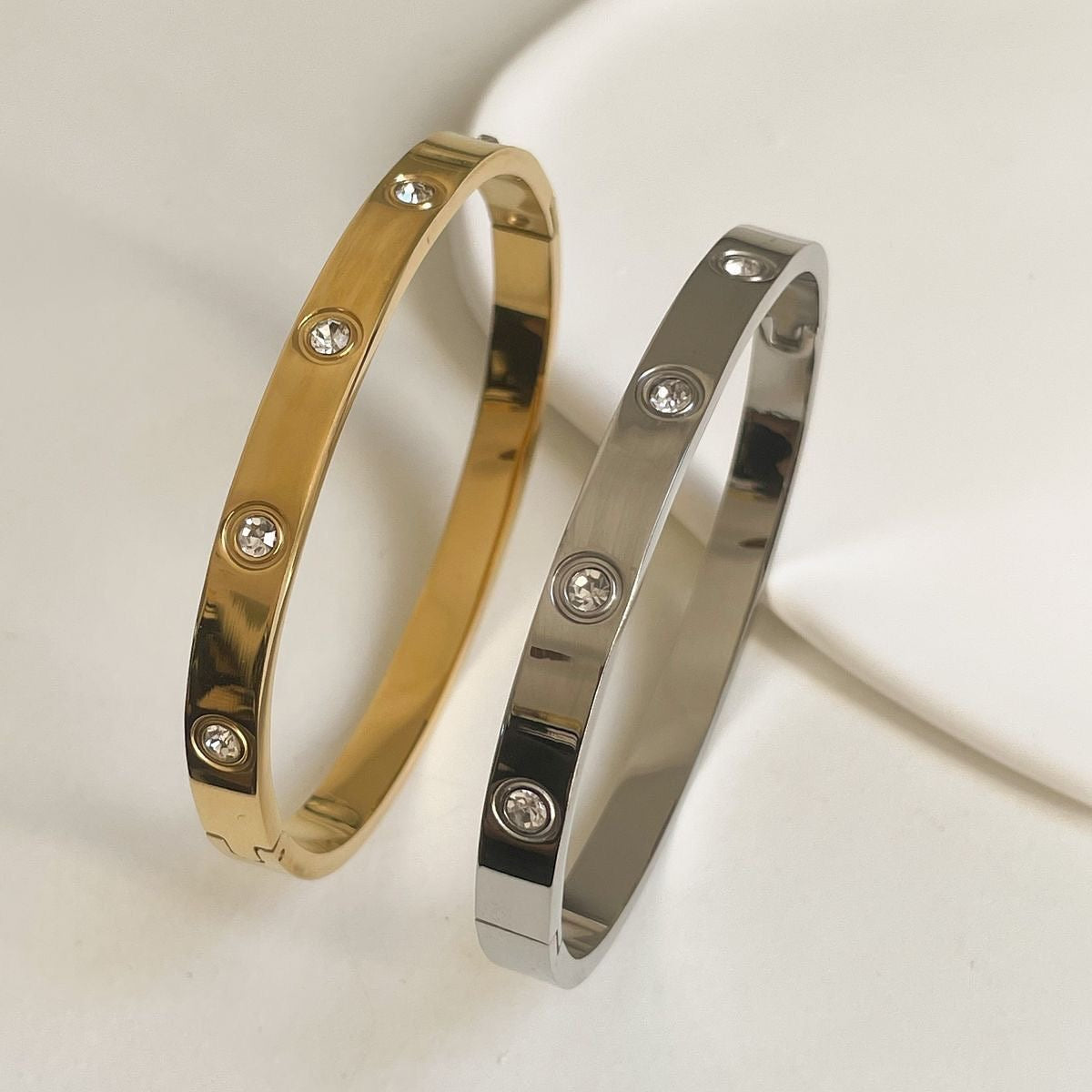 Gold and silver bangles with diamond-like stones on a light background