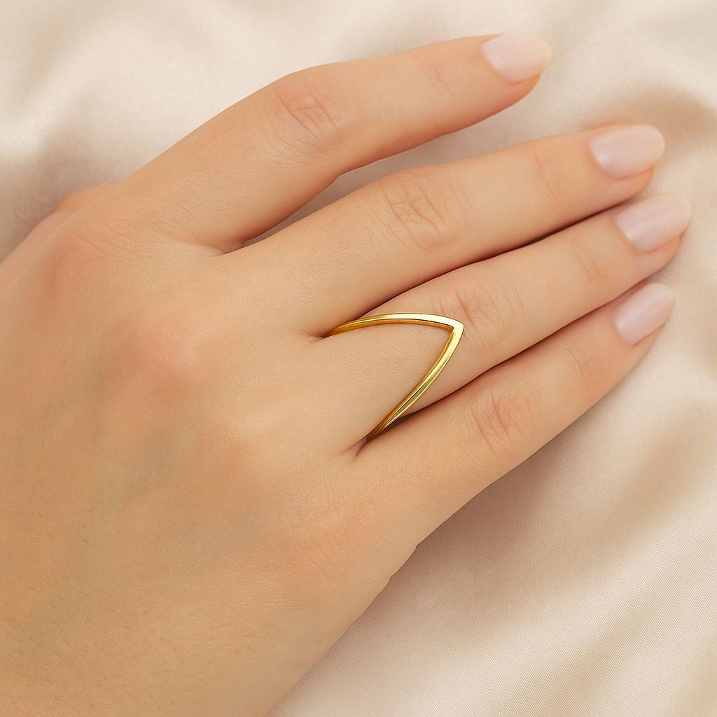 A close-up of a hand wearing a thin, polished gold ring with a curved, open chevron design, resting on a soft beige fabric background.