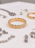A gold bangle bracelet with a continuous raised spiral pattern, displayed on a white surface alongside other jewelry pieces.