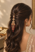 A woman shown from the back wearing a long, ornate gold-toned hair accessory with red and cream stones, paired with matching drop earrings, styled with long dark brown wavy hair.