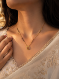A close-up lifestyle shot of a woman wearing a delicate gold necklace with a circular pendant featuring a red floral design, styled with a cream-colored lace garment.
