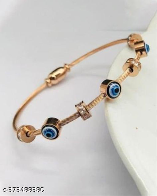 A rose gold wire charm bracelet with evil eye charms and small clear crystal accents, displayed on a white surface.