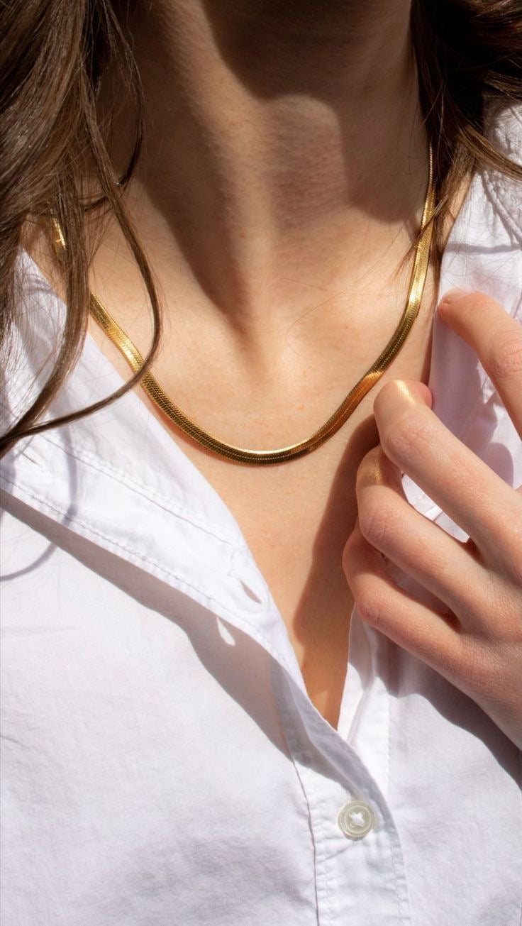 Close-up of a person wearing a gold necklace with a white shirt.